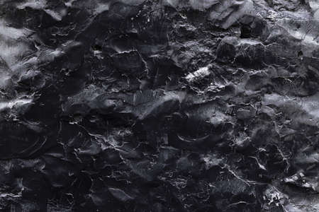A black stone surface with an uneven texture in the form of bulges and cracks in monochrome black tones. Concept background, texture, minimalist black.の写真素材