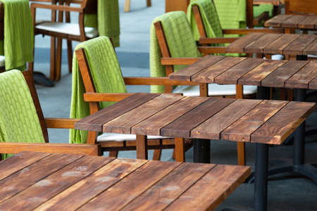 View of a row of empty wooden tables in a street cafe next to which are chairs with green rugs. Concept city, cafe, catering, crisisの写真素材