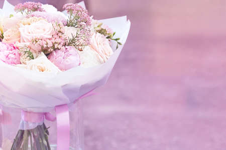 View of a bouquet of flowers from pink peonies and roses in white paper which stands in a glass vase on a pink background. Concept background, flowersの写真素材