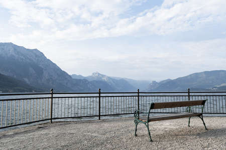 View of an empty bench on a gloomy cloudy day that stands on the embankment of a lake in the mountains. Concept landscape, backgroundの写真素材