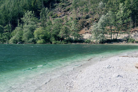 View of a wild beach with white pebble mountain lake with turquoise color of water, cliffs and forest. The concept of nature, mountains, track, travelの写真素材
