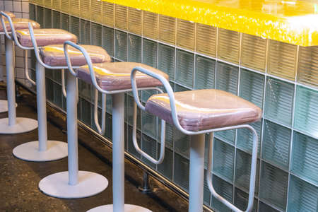 View of a row of bar stools that stand near a bar counter made of glass blocks. Concept interior, business, quarantineの写真素材