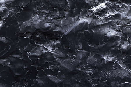 A black stone surface with an uneven texture in the form of bulges and cracks in monochrome black tones. Concept background, texture, minimalist blackの写真素材