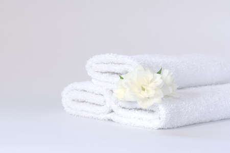 Three white neatly folded terry towels with a jasmine flower on a light backgroundの写真素材