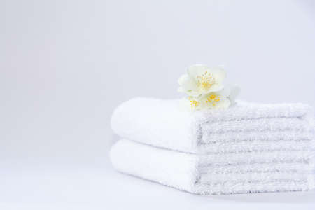 Two white neatly folded terry towels with a jasmine flower on a light backgroundの写真素材