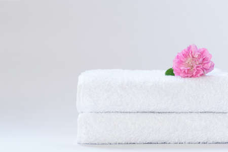 Two white neatly folded terry towels with a rose flower on a light backgroundの写真素材