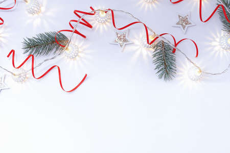 Christmas composition of white shiny stars, a garland of white luminous balls, red ribbons and fir branches on a white background.の写真素材