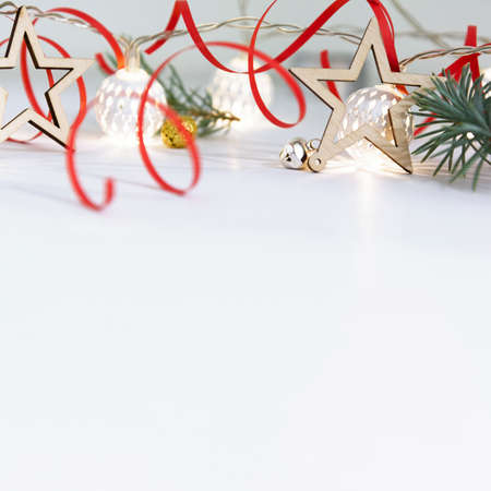 Christmas composition of fir branches, wooden stars, garlands of white luminous balls and red ribbon on a white background.の写真素材