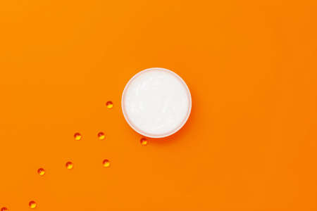 A jar of moisturizing white cream on an orange background next to which are capsules with vitamin E.の写真素材