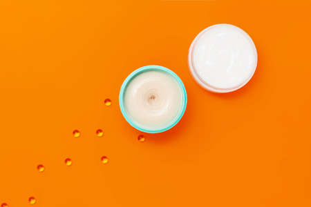 Two jars with different creams on an orange background next to which are capsules with vitamin E.の写真素材