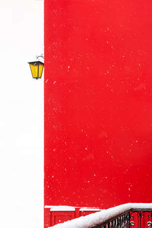 View of a snowy balcony made of forged metal against the background of a red wall of a building during a snowfall and a street lamp. Concept architecture, winter, postcard, christmas, attentionの写真素材