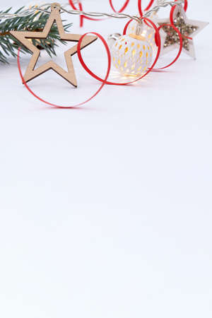 Christmas composition of fir branches, wooden stars, garlands of white luminous balls and red ribbon on a white backgroundの写真素材
