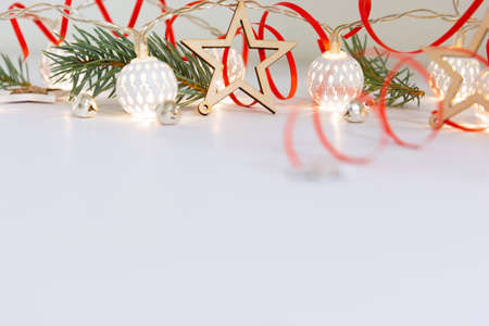 Christmas composition of fir branches, wooden stars, garlands of white luminous balls and red ribbon on a white backgroundの写真素材