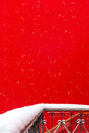View of the snowy balcony and terrace made of forged metal against the background of the red wall of the building during a snowfall. Concept architecture, winter, postcard, christmas, attentionの写真素材