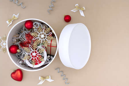 A white round box with Christmas toys next to which are decorations of red, white, gold and silver on a beige backgroundの写真素材