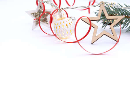 Christmas composition of fir branches, wooden stars, garlands of white luminous balls and red ribbon on a white backgroundの写真素材