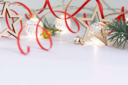 Christmas composition of fir branches, wooden stars, garlands of white luminous balls and red ribbon on a white backgroundの写真素材