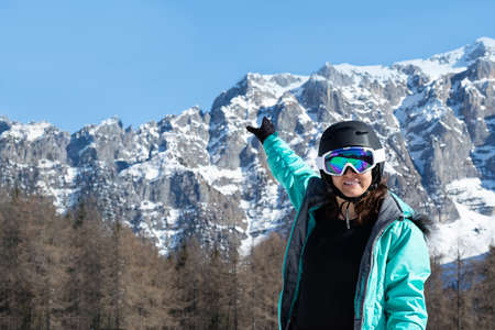 A woman in a colorful ski suit, helmet and sunglasses after skiing stands against the backdrop of mountain peaks. Sports concept, people, travelの写真素材