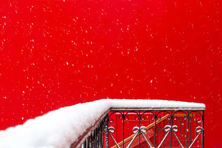 View of the snowy balcony and terrace made of forged metal against the background of the red wall of the building during a snowfall. Concept architecture, winter, postcard, christmas, attentionの写真素材