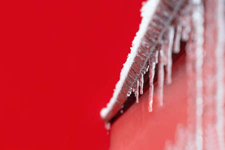 View of the icy windowsill with icicles on the background of the red wall of the building during a snowfall. Concept winter, weather forecast, christmas, dangerの写真素材