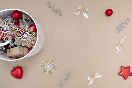 A white round box with Christmas toys next to which are decorations of red, white, gold and silver on a beige backgroundの写真素材