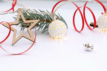 Christmas composition of wooden stars, a garland of white luminous balls, fir branches, bells and a red ribbon on a white backgroundの写真素材