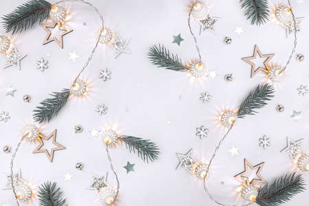 Christmas composition of wooden stars, a garland of white luminous balls, fir branches, bells and snowflakes on a white backgroundの写真素材