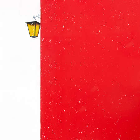 View of a snowy street lamp that hangs on the wall of a red building during a snowfall. The concept of architecture, winter, postcard, Christmas, attention, minimalism.の写真素材