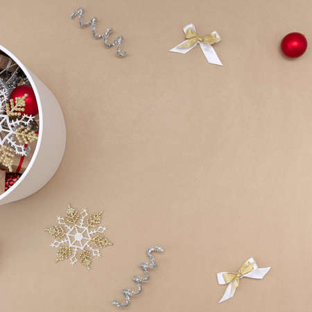 A white round box with Christmas toys next to which are decorations of red, white, gold and silver on a beige background.の写真素材