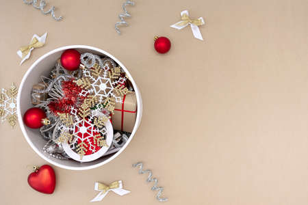 A white round box with Christmas toys next to which are decorations of red, white, gold and silver on a beige background.の写真素材