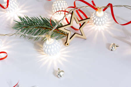 Christmas composition of wooden stars, a garland of white luminous balls, fir branches, bells and a red ribbon on a white background.の写真素材