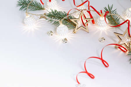 Christmas composition of wooden stars, a garland of white luminous balls, fir branches, bells and a red ribbon on a white background.の写真素材
