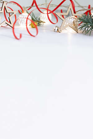 Christmas composition of fir branches, wooden stars, garlands of white luminous balls and red ribbon on a white background.の写真素材