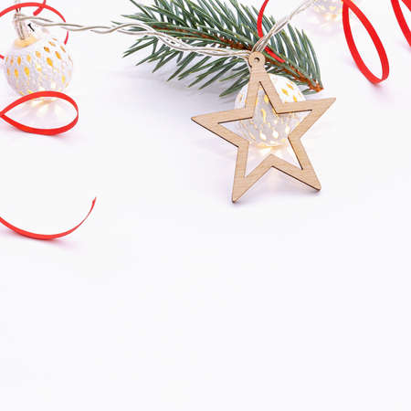 Christmas composition of fir branches, wooden stars, garlands of white luminous balls and red ribbon on a white backgroundの写真素材