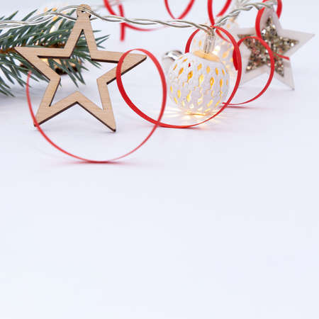 Christmas composition of fir branches, wooden stars, garlands of white luminous balls and red ribbon on a white backgroundの写真素材