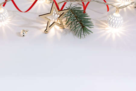 Christmas composition of fir branches, wooden stars, garlands of white luminous balls and red ribbon on a white backgroundの写真素材