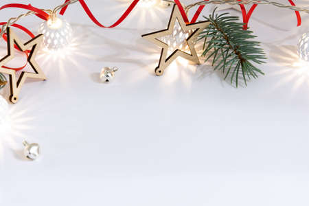 Christmas composition of wooden stars, a garland of white luminous balls, fir branches, bells and a red ribbon on a white backgroundの写真素材