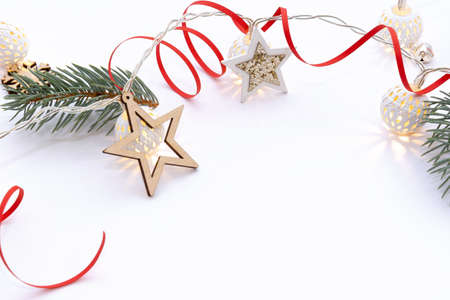Christmas composition of fir branches, wooden stars, garlands of white luminous balls and red ribbon on a white backgroundの写真素材