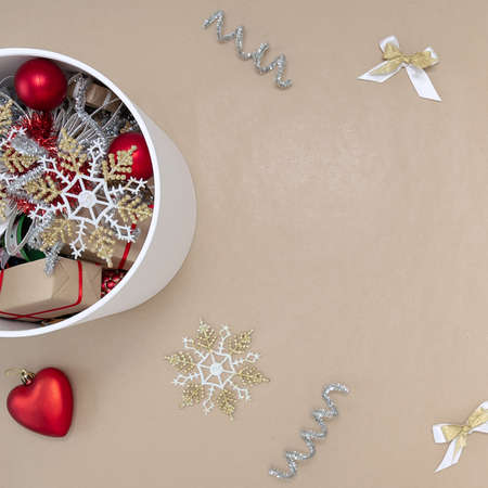 A white round box with Christmas toys next to which are decorations of red, white, gold and silver on a beige backgroundの写真素材