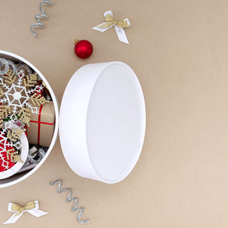 A white round box with Christmas toys next to which are decorations of red, white, gold and silver on a beige backgroundの写真素材