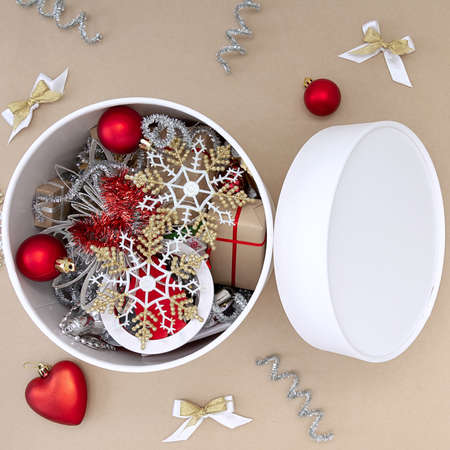 A white round box with Christmas toys next to which are decorations of red, white, gold and silver on a beige backgroundの写真素材