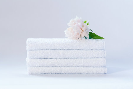 Four white neatly folded terry towels with a delicately pink peony flower on a light backgroundの写真素材
