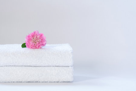 Two white neatly folded terry towels with a rose flower on a light backgroundの写真素材