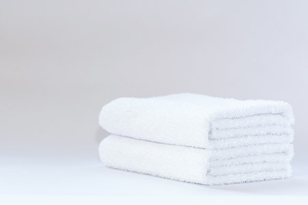 Two white neatly folded terry towels on a light backgroundの写真素材