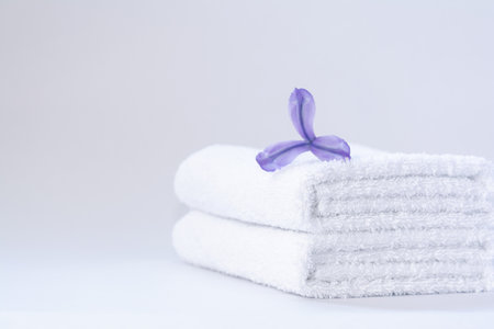 Two white neatly folded terry towels with a purple iris flower on a light backgroundの写真素材
