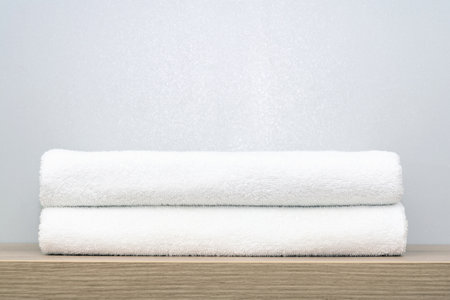 A view of two neatly folded white bath towels on a wooden shelfの写真素材