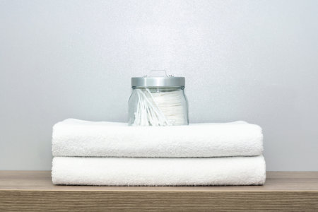 A view of a glass jar of personal hygiene items that stands on two neatly folded towelsの写真素材