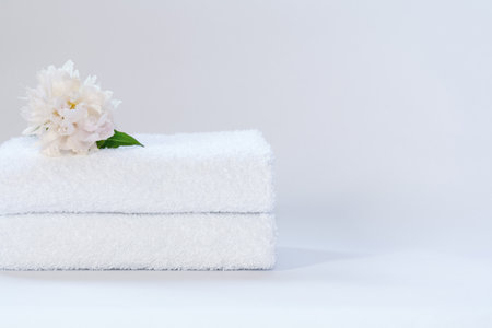 Two white neatly folded terry towels with a delicately pink peony flower on a light backgroundの写真素材