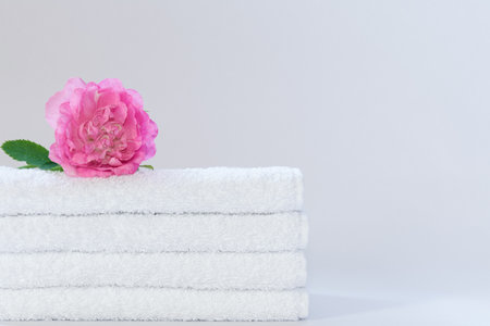 Four white neatly folded terry towels with a rose flower on a light backgroundの写真素材