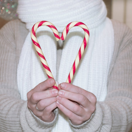 An adult married woman in a beige sweater and white scarf holds Christmas candies in the form of a heart.の写真素材